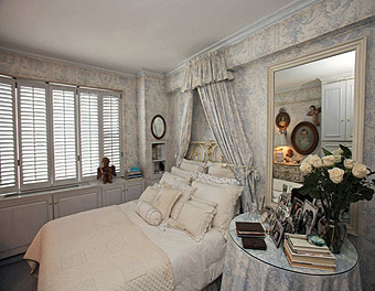 غرفة نوم استعملت فيها ليك مفارش بيضاء بأسلوب قديم وسرير بجوانب من نحاس وتكرر في الغرفة اللونان الأبيض والأزرق المتدرج إلى الرمادي، سواء في ورق الجدران أو الستائر والنوافذ 